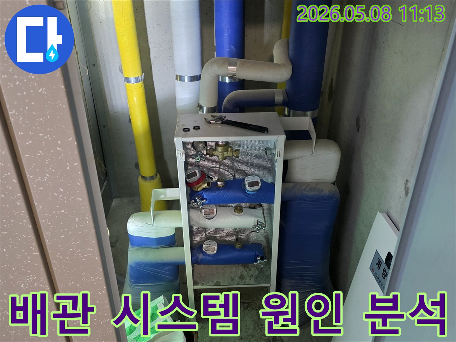 이 이미지는 건물의 유틸리티 공간에 있는-다양한 색상의 단열재로 감싸진 배관과-수도 계량기-그리고 작업 도구를 보여주며-이는 누수 원인 분석을 위한-전문적인 점검 과정을 나타냅니다