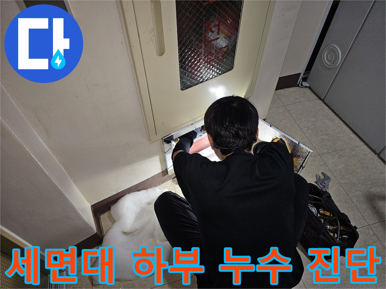 세면대 아래쪽의 좁은 공간에서 엔지니어가 배관 연결 부위를 점검하고 있습니다.