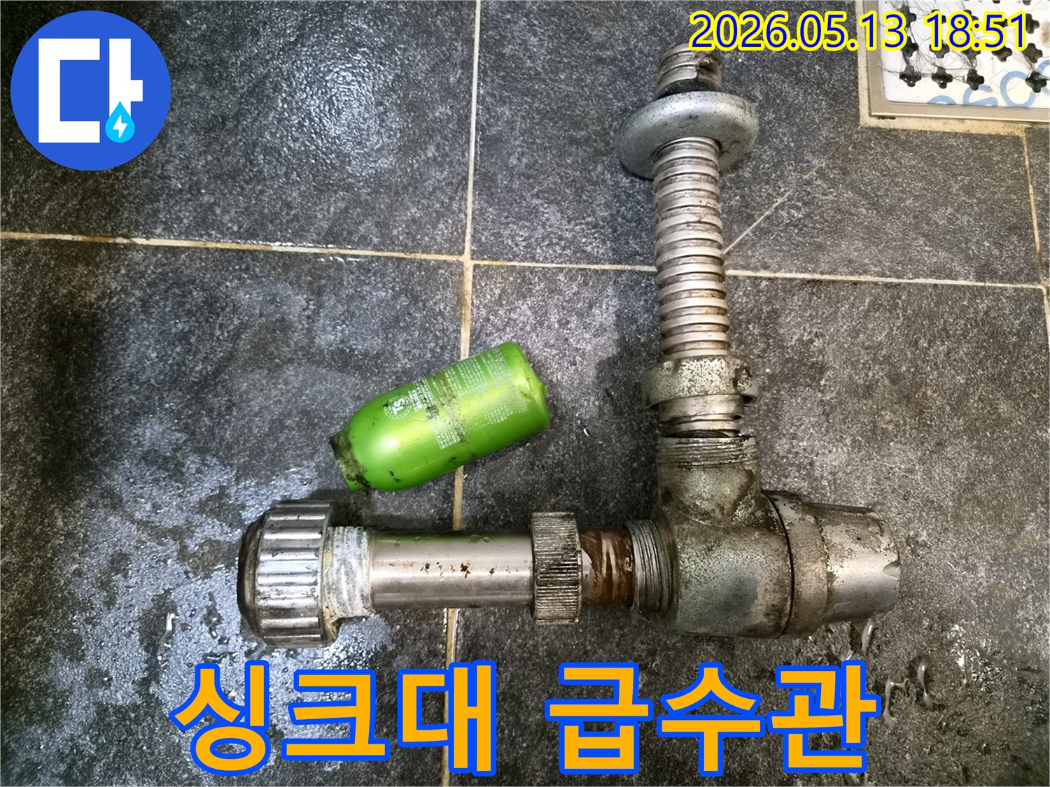 어두운 타일 바닥 위에-분리된 싱크대 급수관 부품과-초록색 세제통이 놓여있는-누수 수리 현장 기록