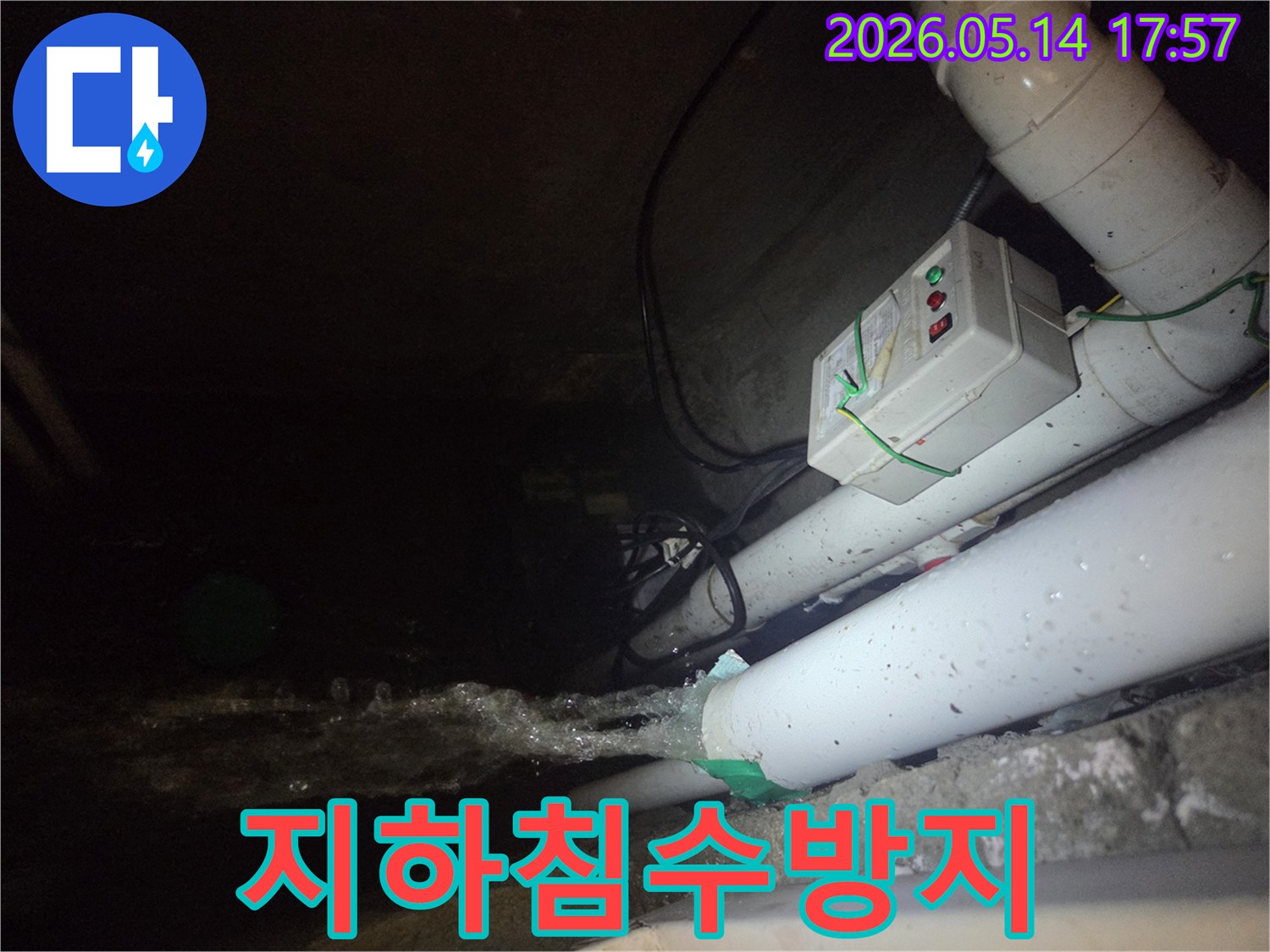 어두운 지하 공간에서-파이프에서 물이 강하게 뿜어져 나오는-심각한 누수 현장을 보여주는 사진입니다-전기 제어 박스와 배관들이 함께 보입니다.
