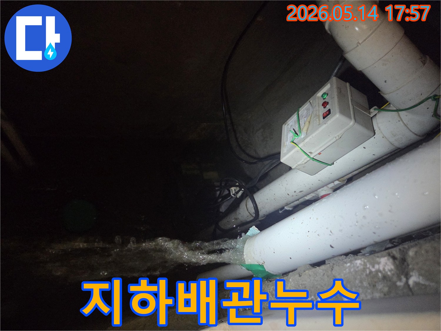 어두운 지하 공간에서-파이프에서 물이 힘차게 뿜어져 나오는-누수 현장을 보여주는 이미지입니다-전기 제어 박스와 배관들이 보입니다.