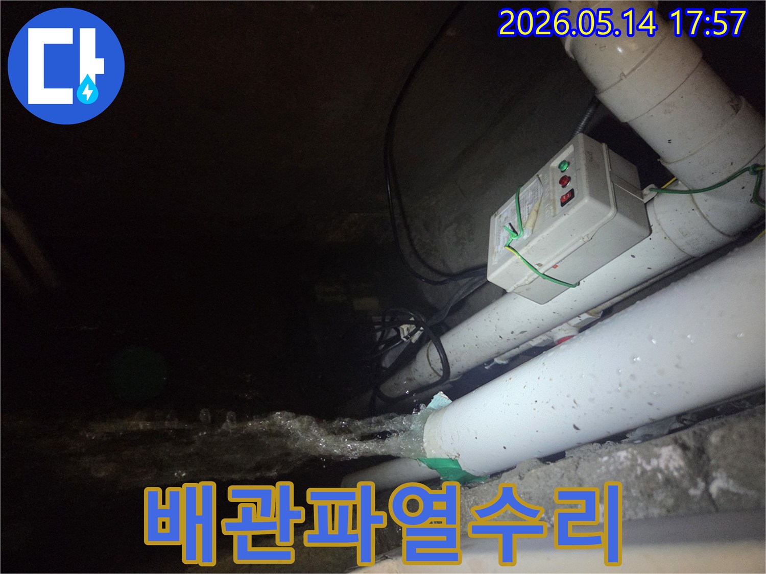 지하 배관에서 물이 새어 나와-바닥으로 흘러내리는 긴급한 누수 상황을 포착한 사진입니다-주변에는 배관과 전기 장치가 있습니다.