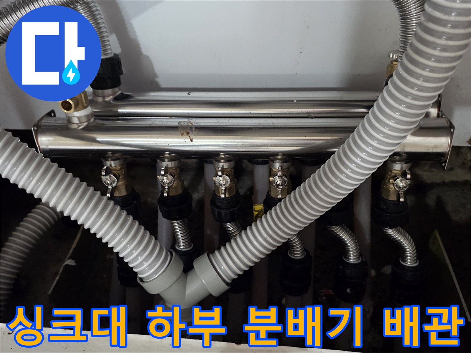 주방 싱크대 하단에 설치된 보일러 분배기와 연결된 은색 주름관 모습입니다.