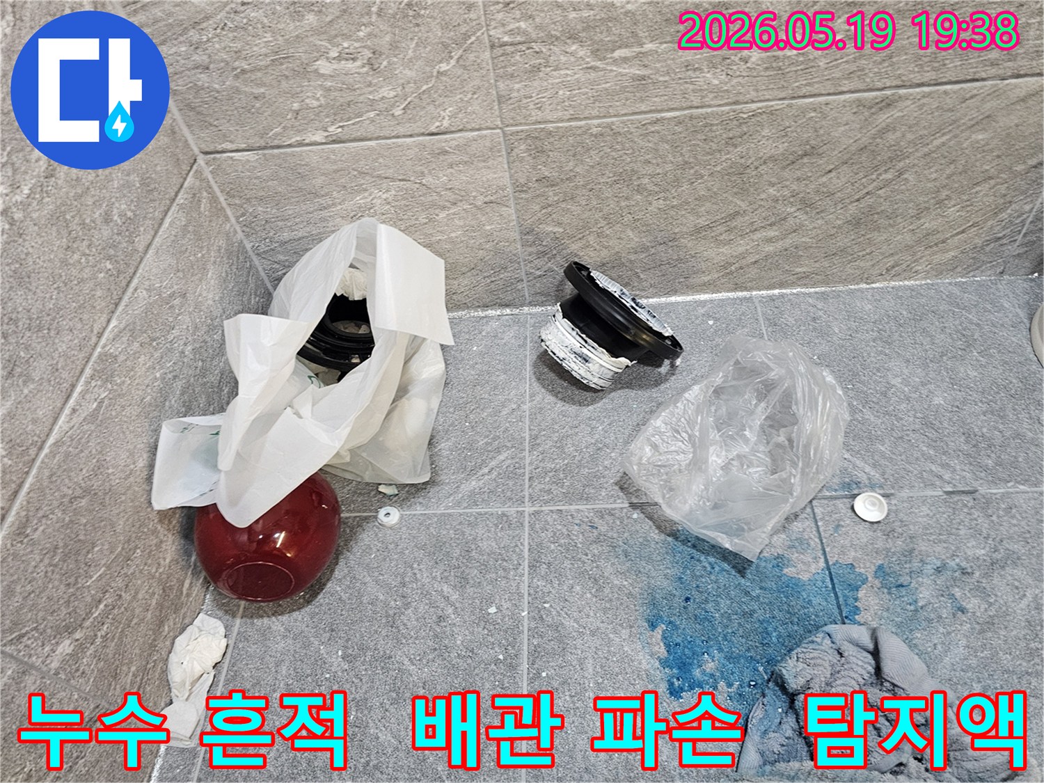 누수 탐지 중-파란색 탐지액이 바닥에 퍼져 있으며-주변에는 손상된 배관 부품들이 놓여 있는 현장 사진입니다