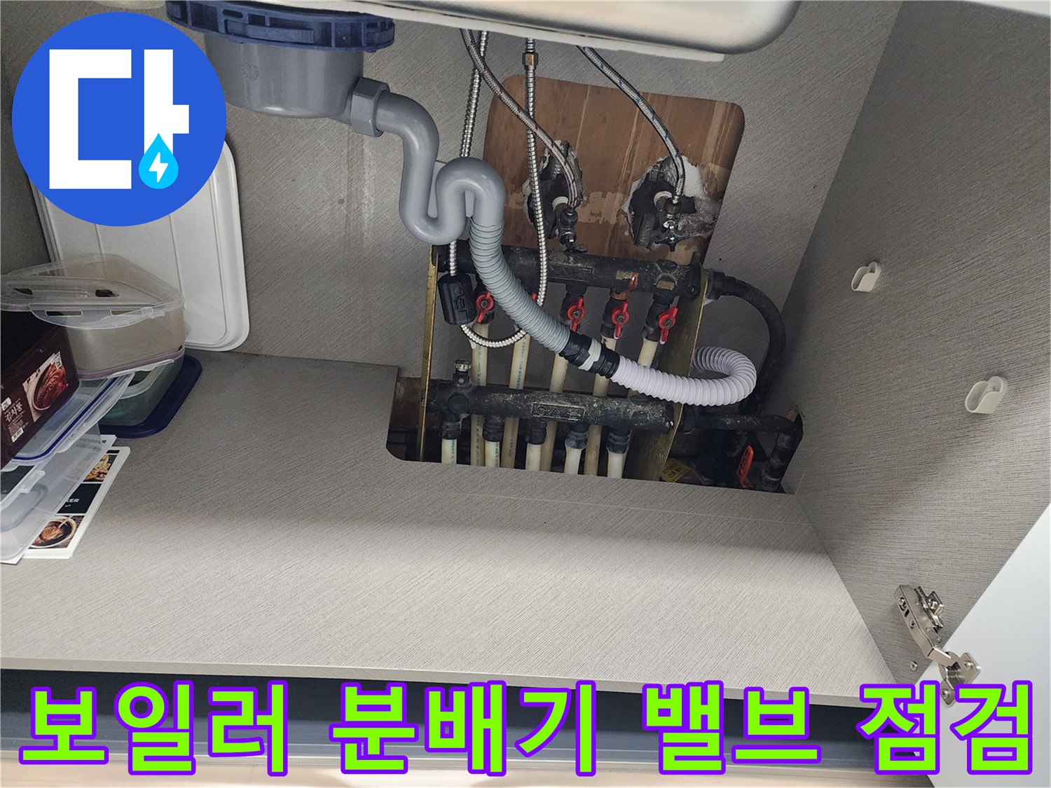 분배기 밸브와 배관이 연결된 싱크대 하부장 내부 모습