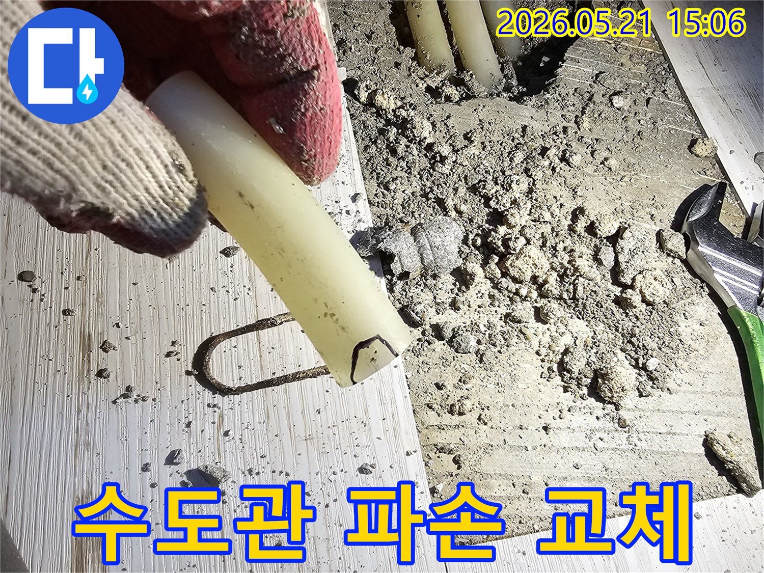 작업 장갑을 낀 손이 파손된 수도관 조각을 들고-교체 작업을 설명하는-현장 사진입니다