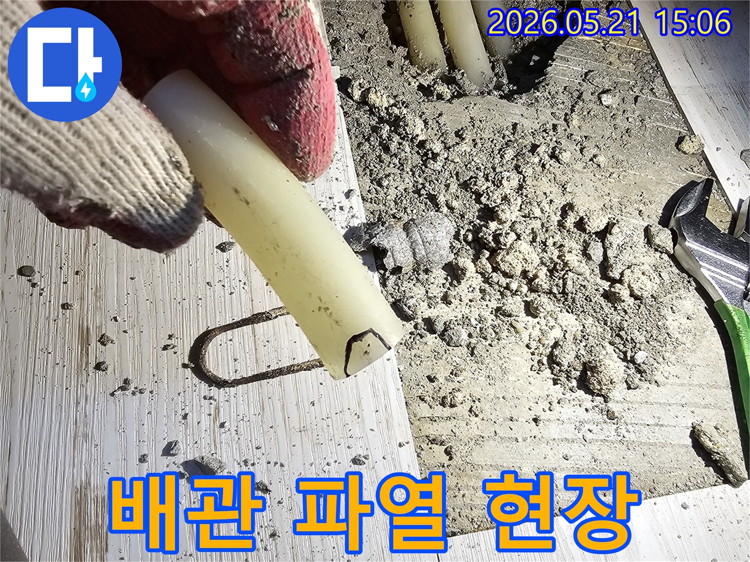 작업용 장갑을 낀 손이 파열된 배관 조각을 들고-누수 지점을 보여주는-공사 현장 사진입니다