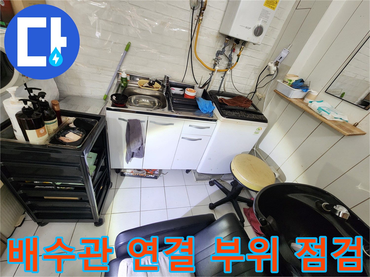 싱크대 하부장 주변의 세탁기 호스와 배수관 접합부를 정밀하게 진단하는 장면