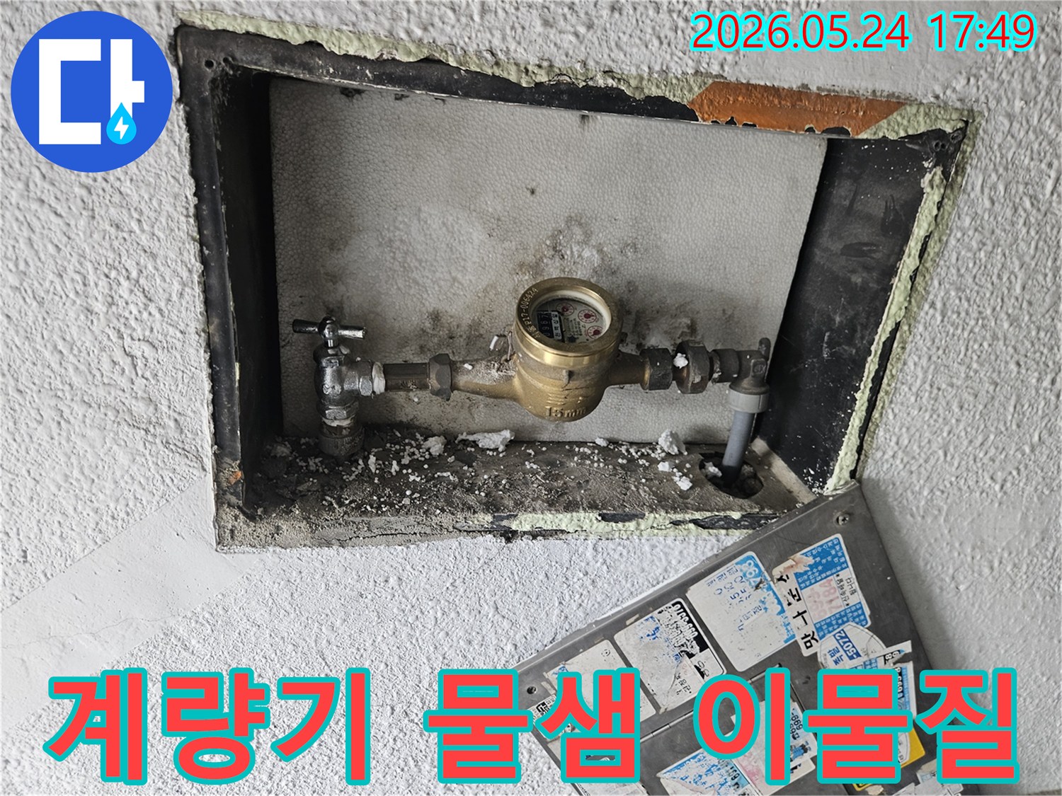 수도 계량기 주변에 쌓인 이물질과-함께 물샘으로 인한-백화 현상이 관찰되는 사진입니다.