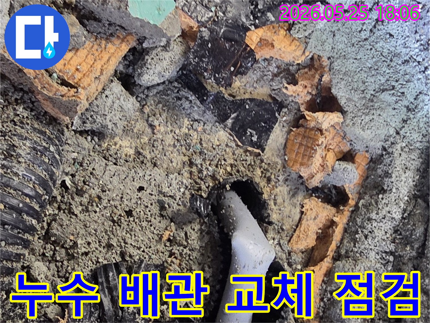 파쇄된 바닥 아래에서 발견된 젖은 배관과 주변의 흙-콘크리트 조각들은-누수 수리를 위한 배관 교체 작업을 보여줍니다.