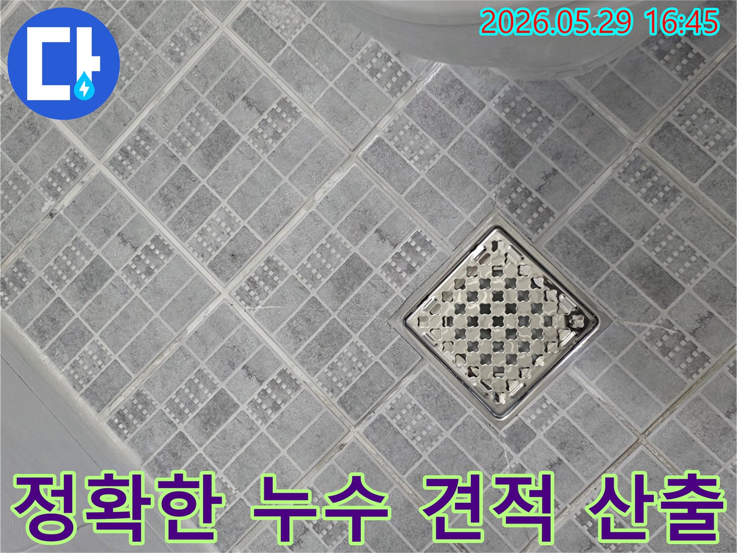 욕실 바닥의 회색 타일과-중앙의 스테인리스 배수구-그리고 변기 하단부가 보이는-누수 견적 산출을 위한 현장 점검