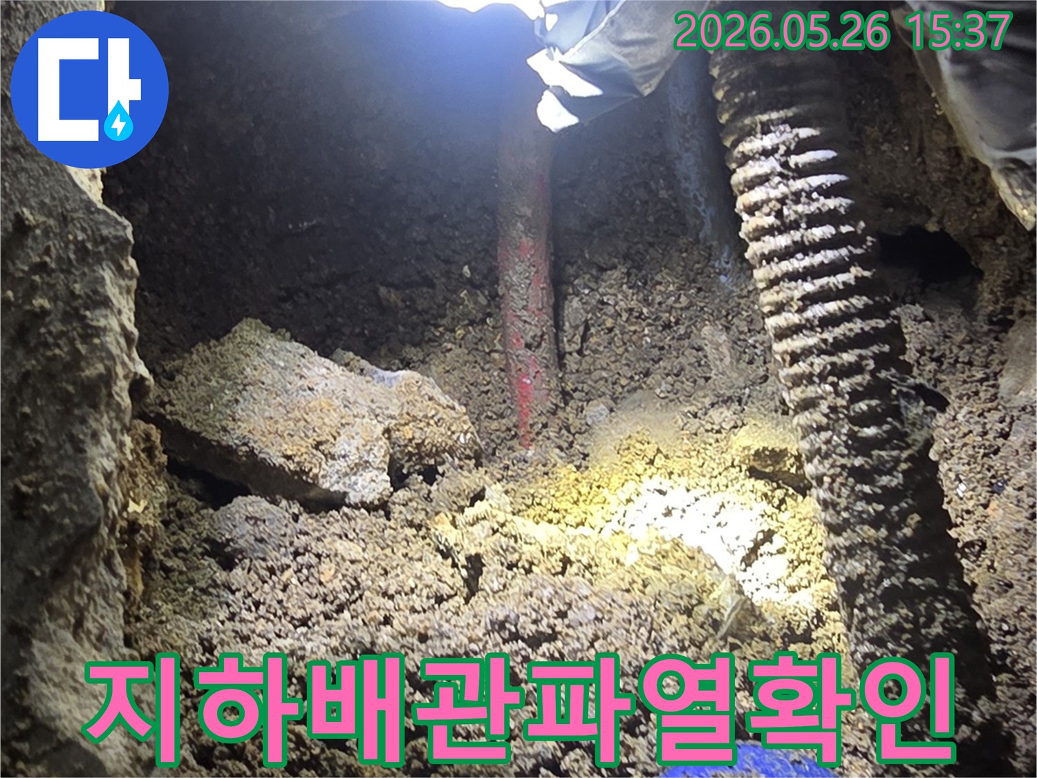 누수-탐지-전문가가-어두운-굴착-현장에서-지하-배관의-파열-지점을-손전등으로-밝혀-확인하는-모습