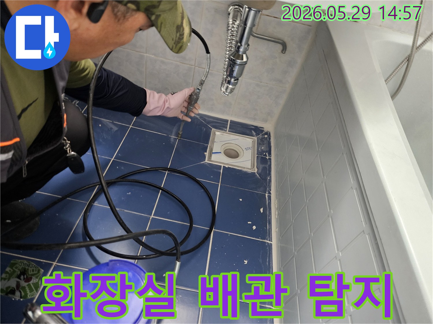 전문가가 분홍색 장갑을 끼고 욕실 바닥 배수구에 연결된 호스를 조작하며 누수 지점을 찾아내는 장면입니다-정확한 진단을 위한 필수적인 작업입니다