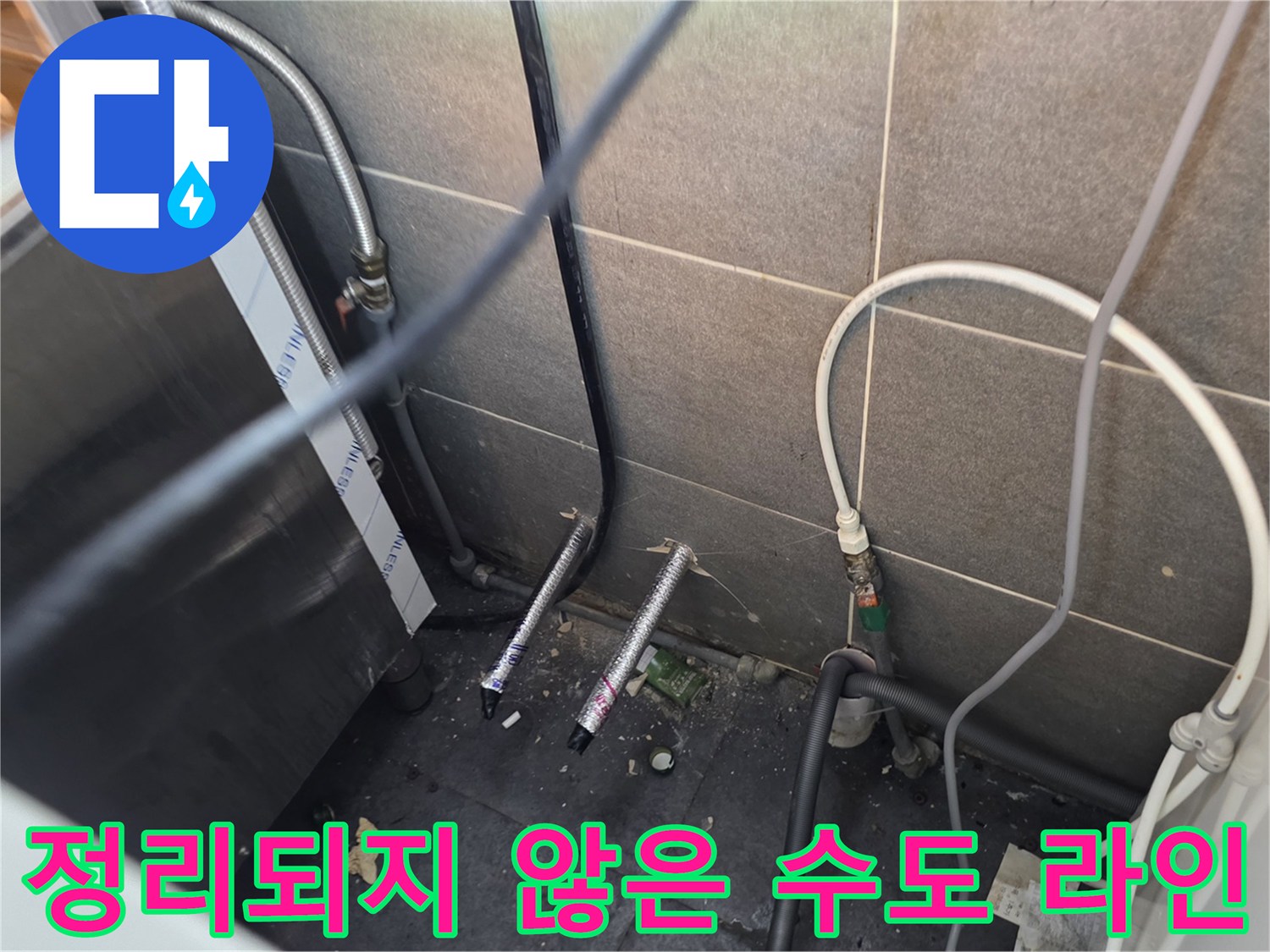 주방 하단부의 어지러운 배관들과 벽면 타일 경계 부위