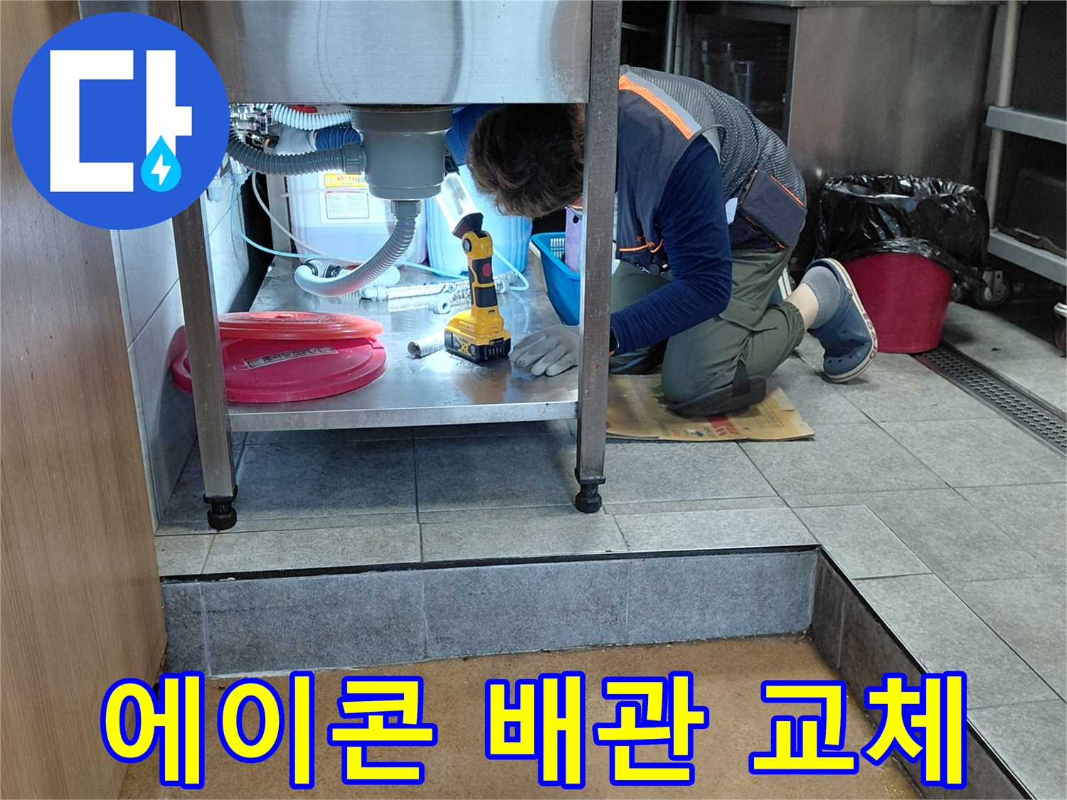 좁은 싱크대 하단 공간에서 에이콘 파이프 연결 부위를 수선하는 엔지니어의 작업 모습입니다.