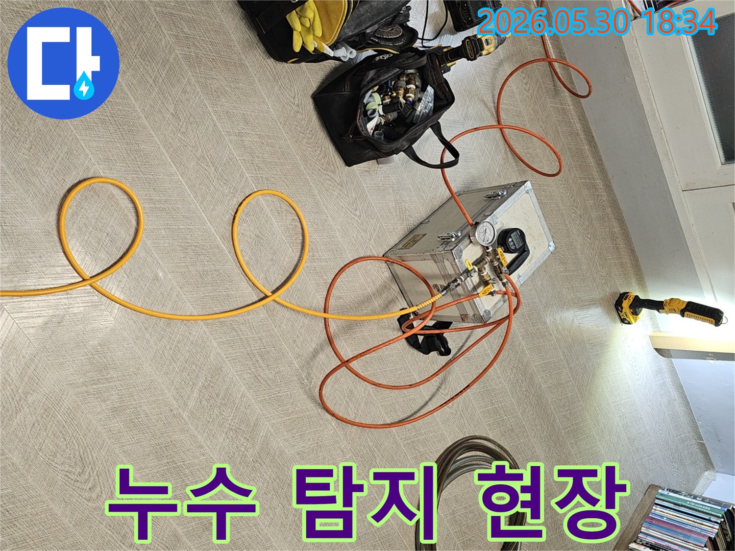 실내 바닥에 설치된 누수 탐지 장비와-다양한 연결 호스-그리고 작업 도구들이-누수 진단을 위해 준비된 장면입니다.