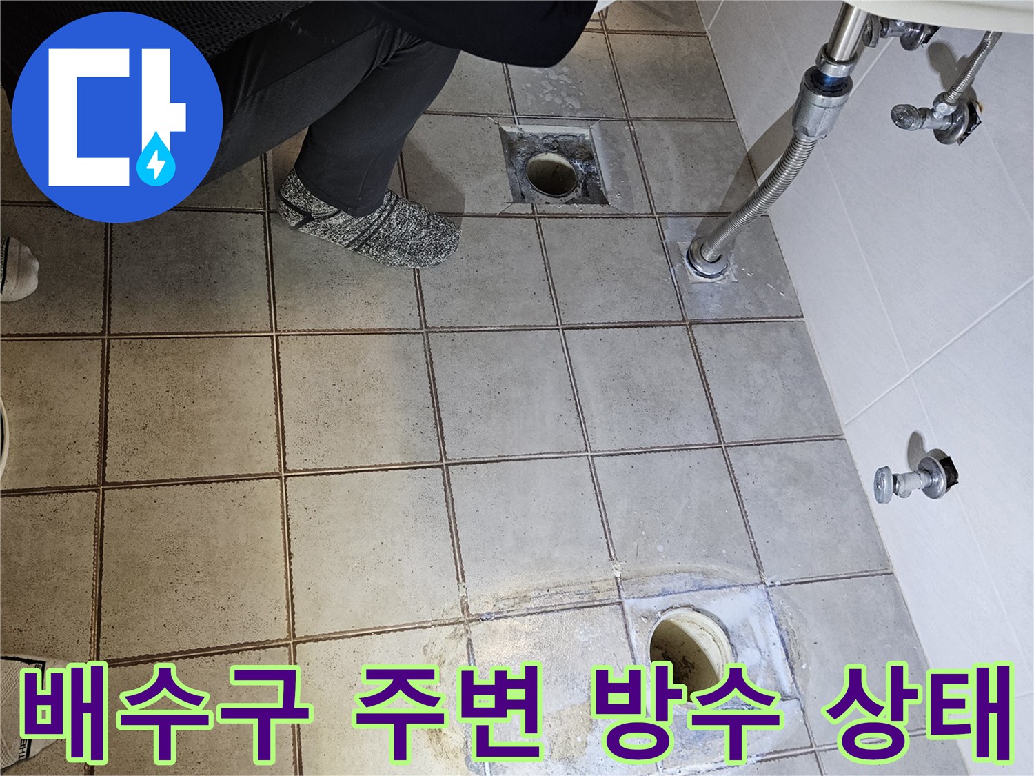 화장실 배수구와 변기 배관 주변의 노후된 타일 상태를 보여주는 사진입니다.