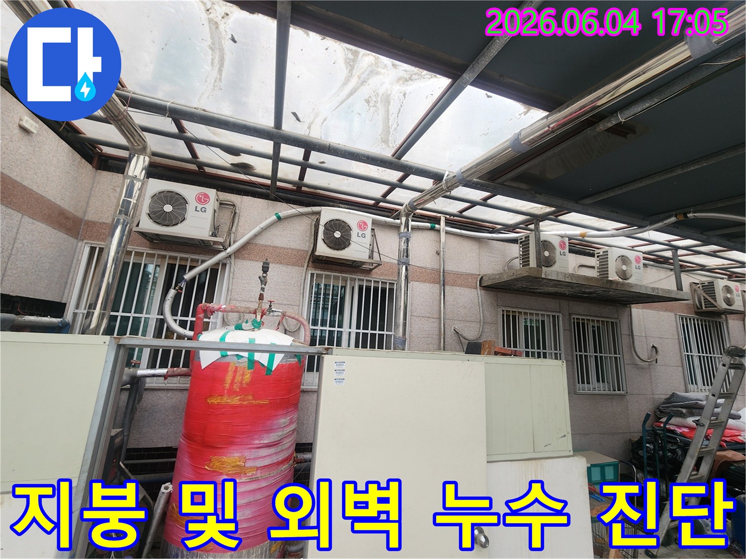 이 사진은 투명한 지붕 구조물과-그 아래 건물 외벽-그리고 다양한 외부 설비들이 있는 공간을 보여줍니다