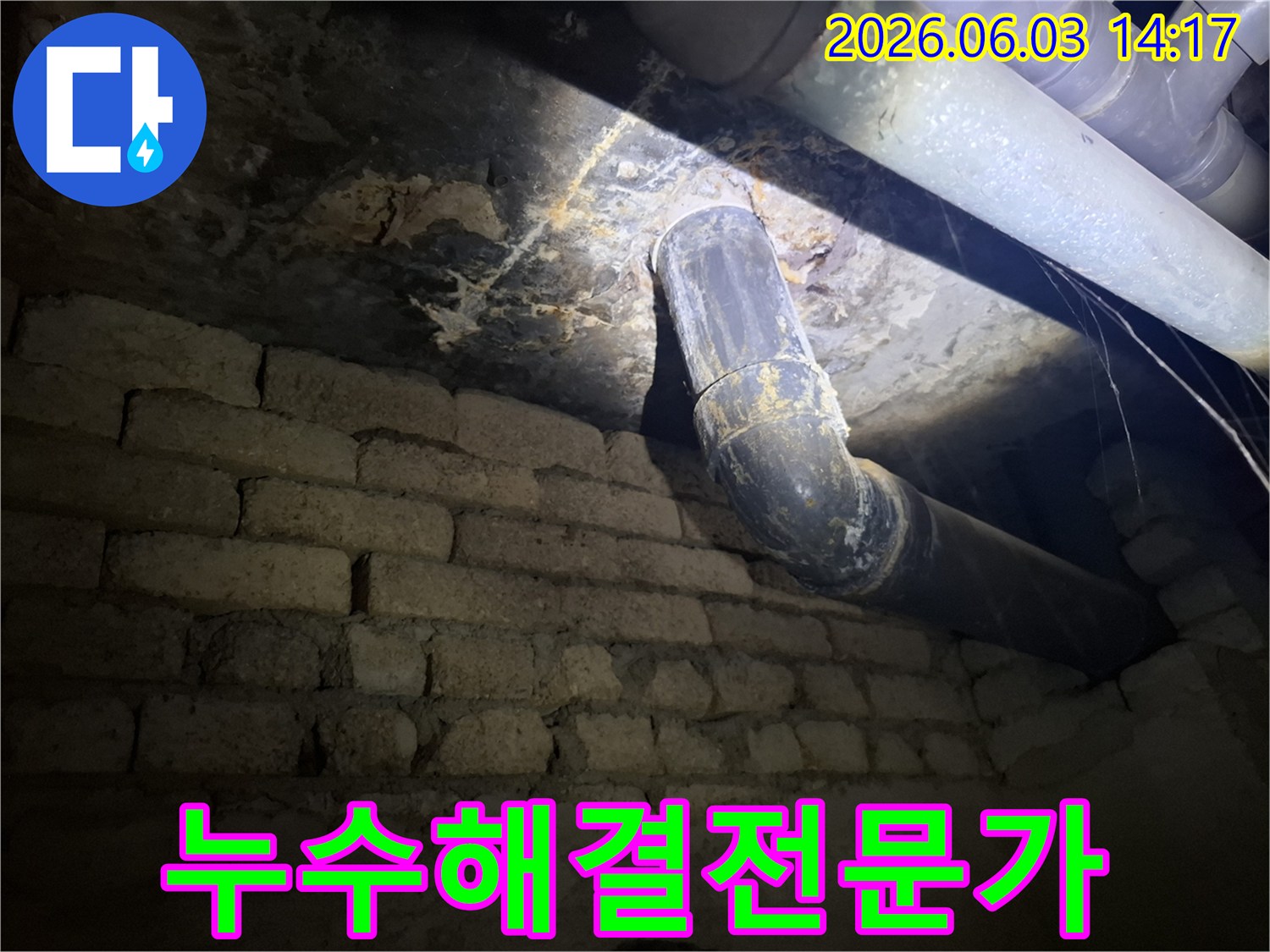 어두운 지하 공간의-낡은 벽돌 벽과-오래된 배관 주변에서-발견된 누수 흔적을-조명으로 비추어-정밀하게 진단하는 모습