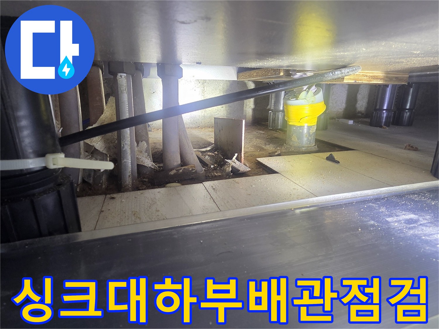 주방 싱크대 하부의 복잡한 배관과 연결 부위를 정밀하게 점검하는 모습입니다.
