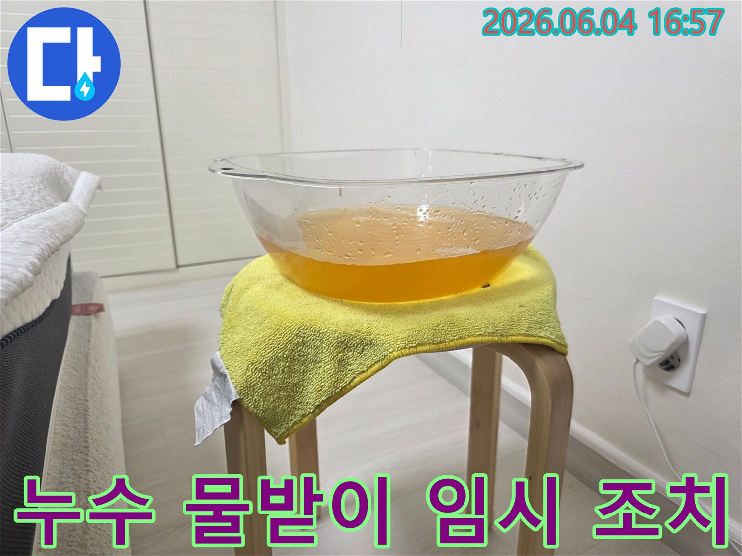 천장 누수 발생 시-추가적인 물 피해를 막기 위해-설치된 임시 물받이와-그 아래 노란 수건의 모습