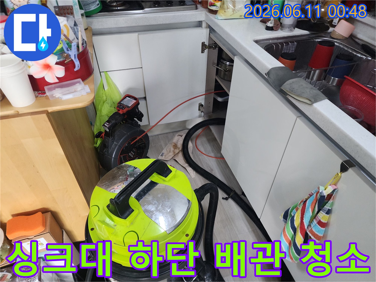 석션 장비를 사용하여 싱크대 하부 배관을 청소하는 장면입니다.