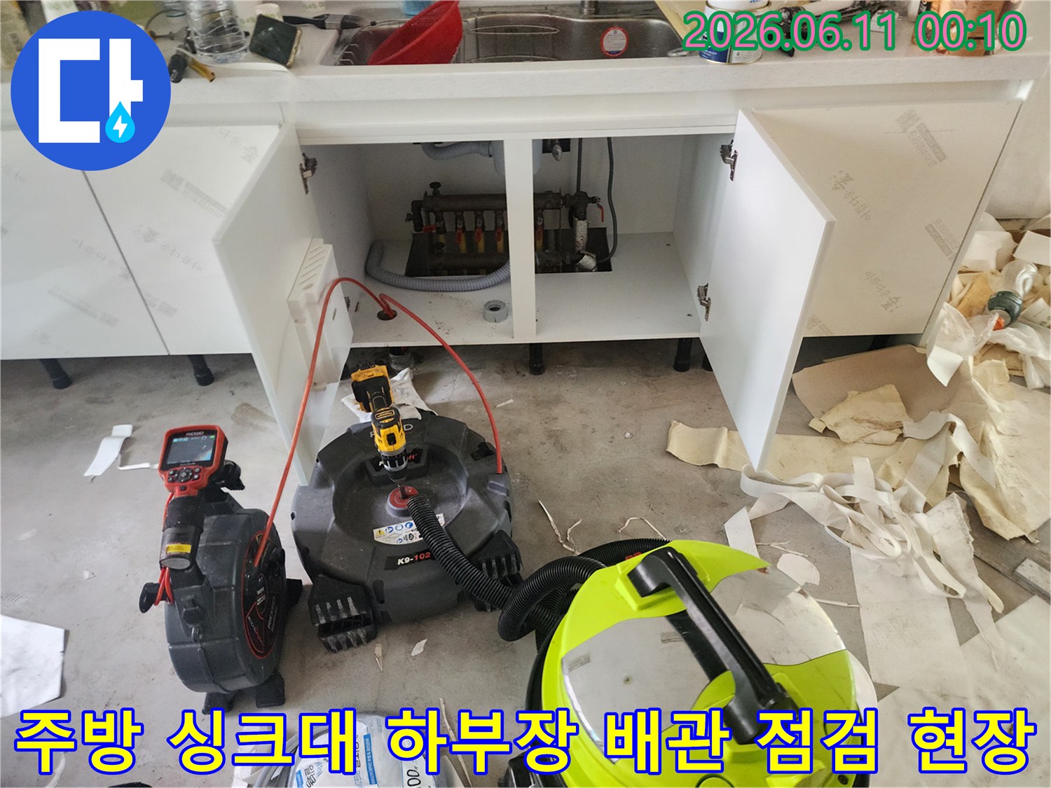 막힌 배관을 뚫기 위해 준비된 전문 석션 장비와 작업 중인 싱크대 하부장
