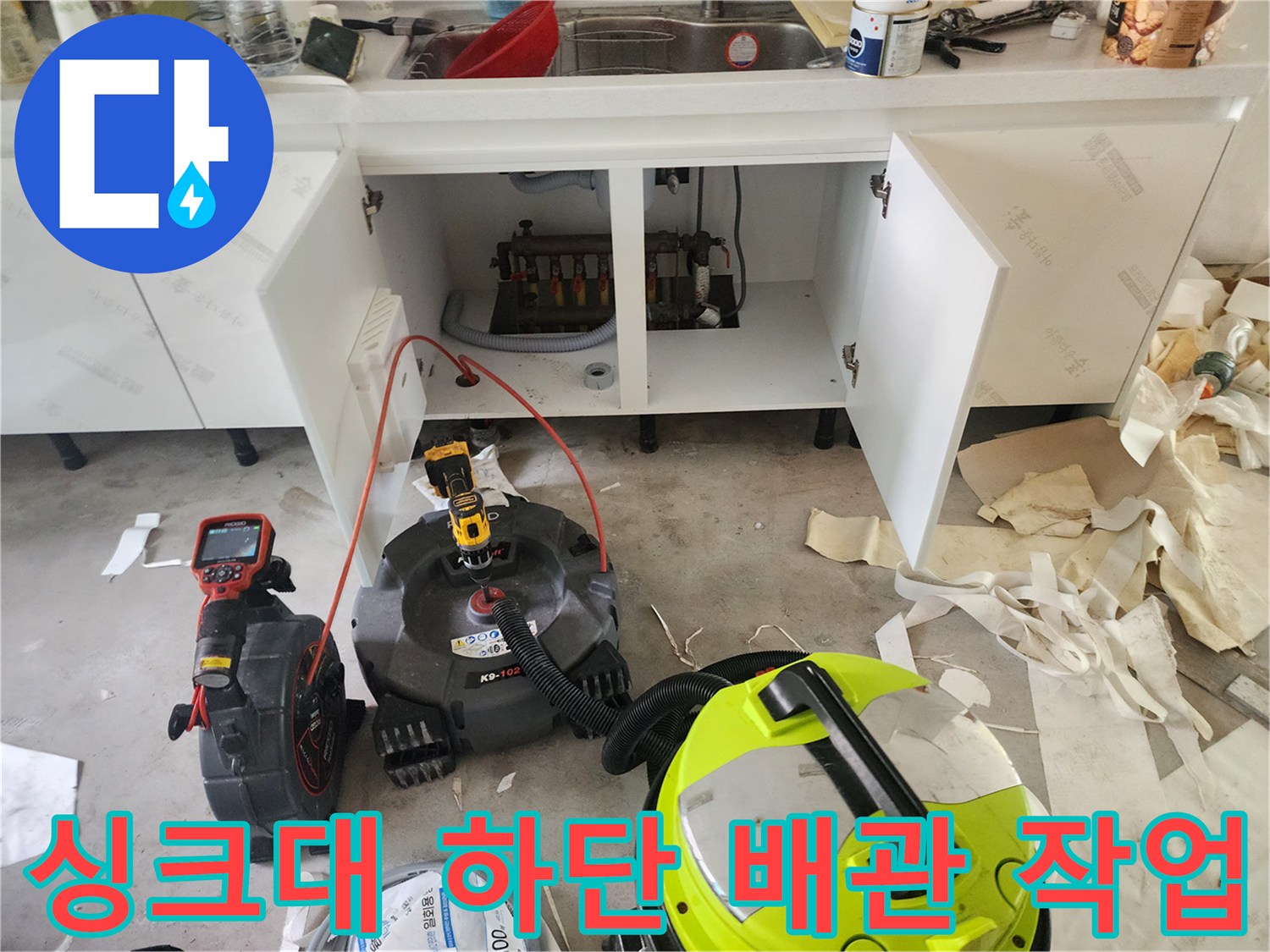 인테리어 공사 중인 주방 싱크대 하부장 아래 배관 청소 장비가 놓여 있습니다.