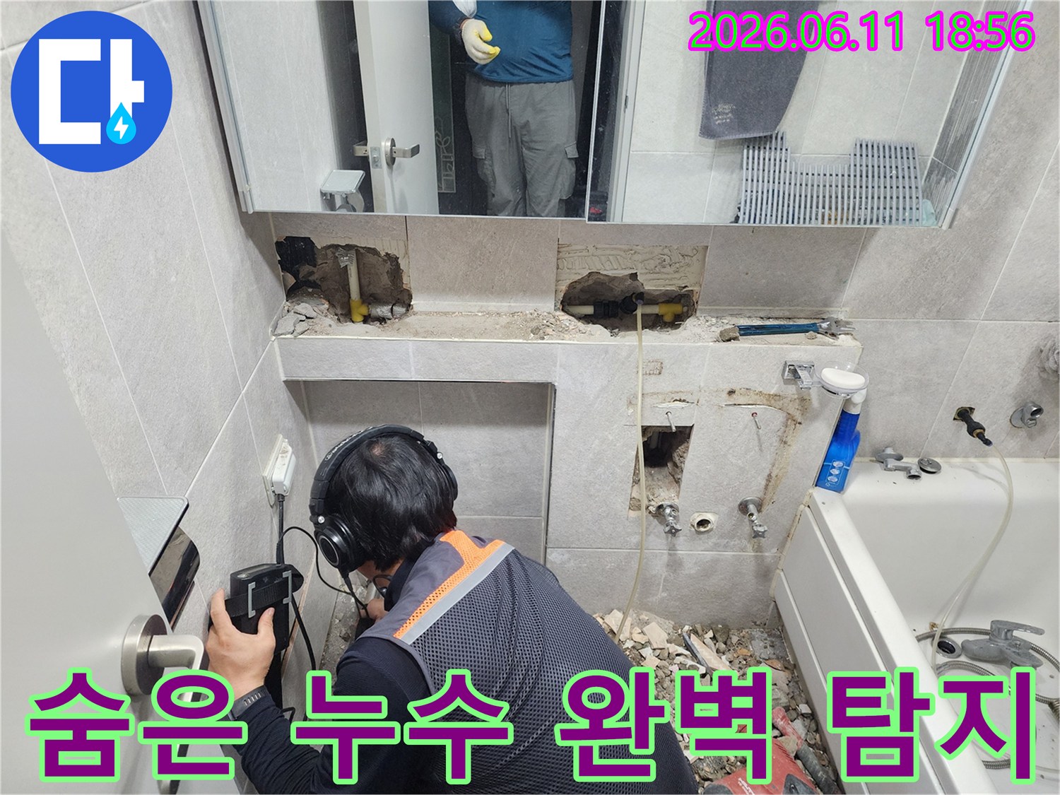 전문가가-누수 탐지 장비를 사용하여-욕실 벽면의-미세한 누수음을 듣고 있는 현장