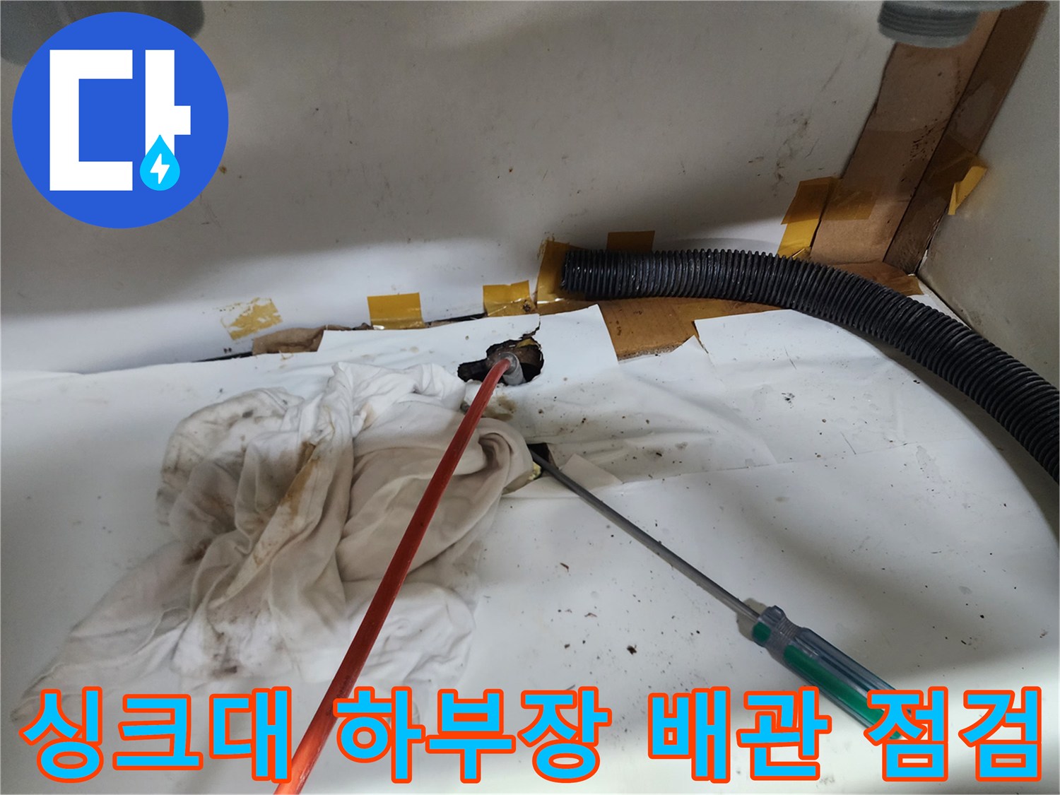 하부장 바닥에 배치된 작업 도구와 오염된 배관 입구의 근접 촬영