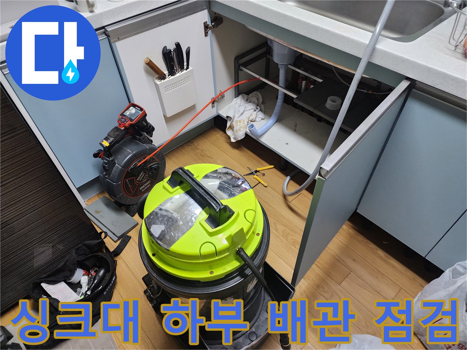 하부장 내부의 싱크대 배관과 청소용 석션 장비 모습