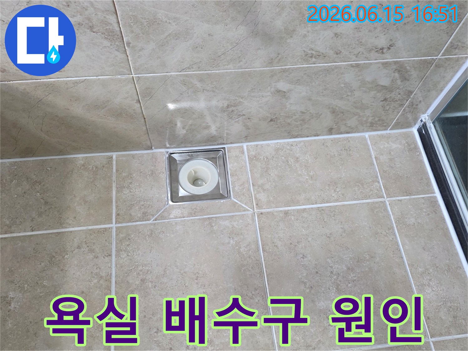 깨끗하게 시공된 욕실 타일 중앙에-사각형 배수구가 위치하며-주변 마감 상태를 면밀히 관찰하는 사진입니다