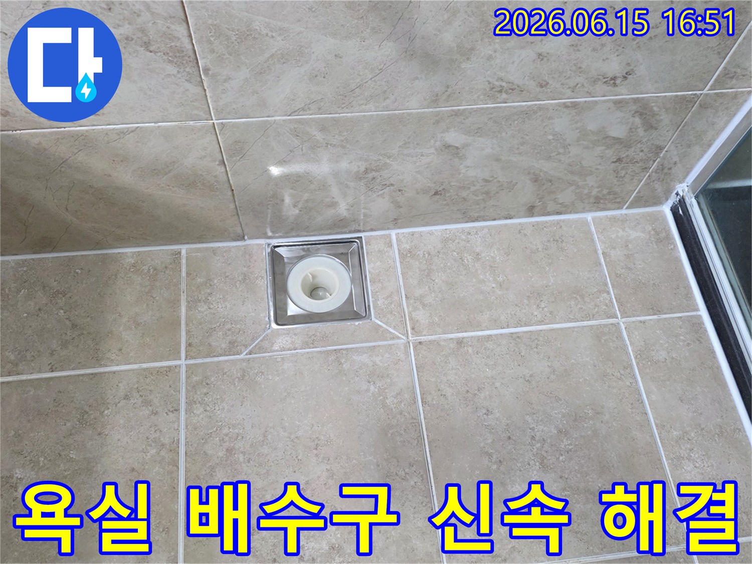 깨끗하게 시공된 욕실 타일 중앙에-사각형 배수구가 위치하며-주변 마감 상태를 면밀히 관찰하는 사진입니다