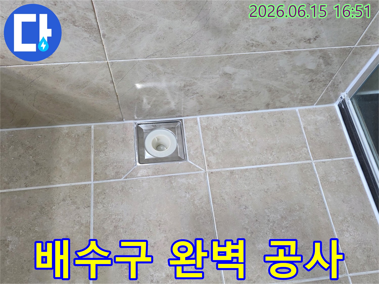 베이지색 타일 바닥에 설치된-금속 사각 배수구의 모습으로-주변 타일과 줄눈의 마감 상태를 보여줍니다