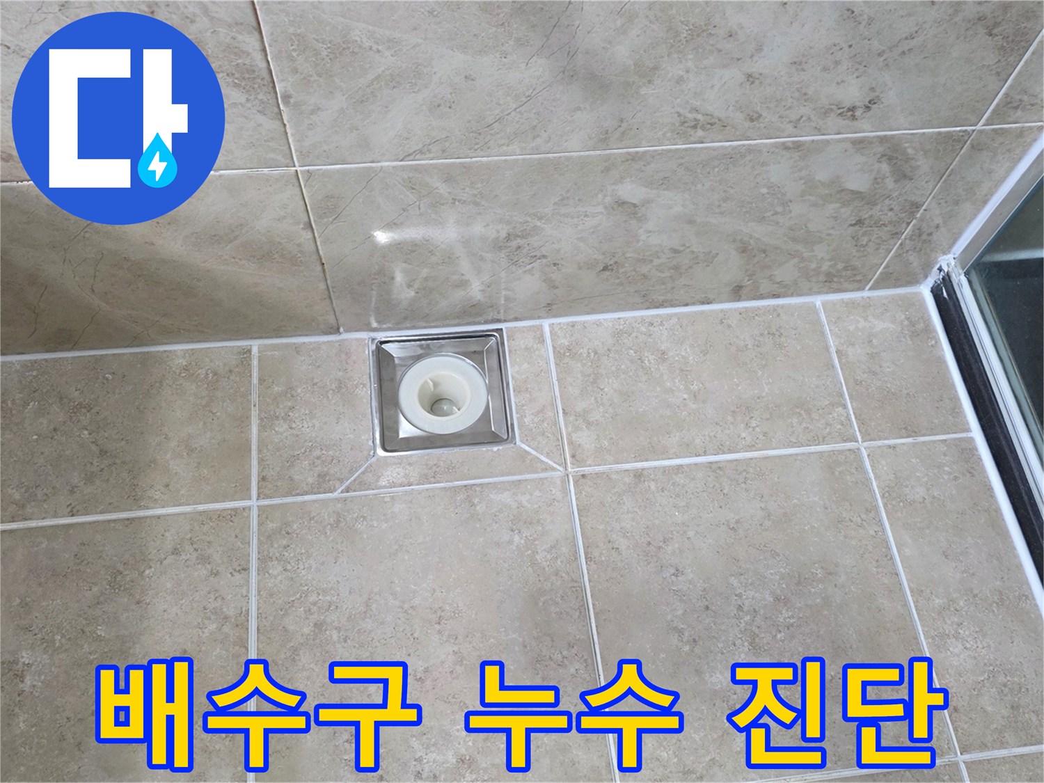 베이지색 타일 바닥에 설치된-사각형 금속 배수구의 모습으로-주변 타일과 줄눈의 상태를 면밀히 관찰하는 이미지입니다
