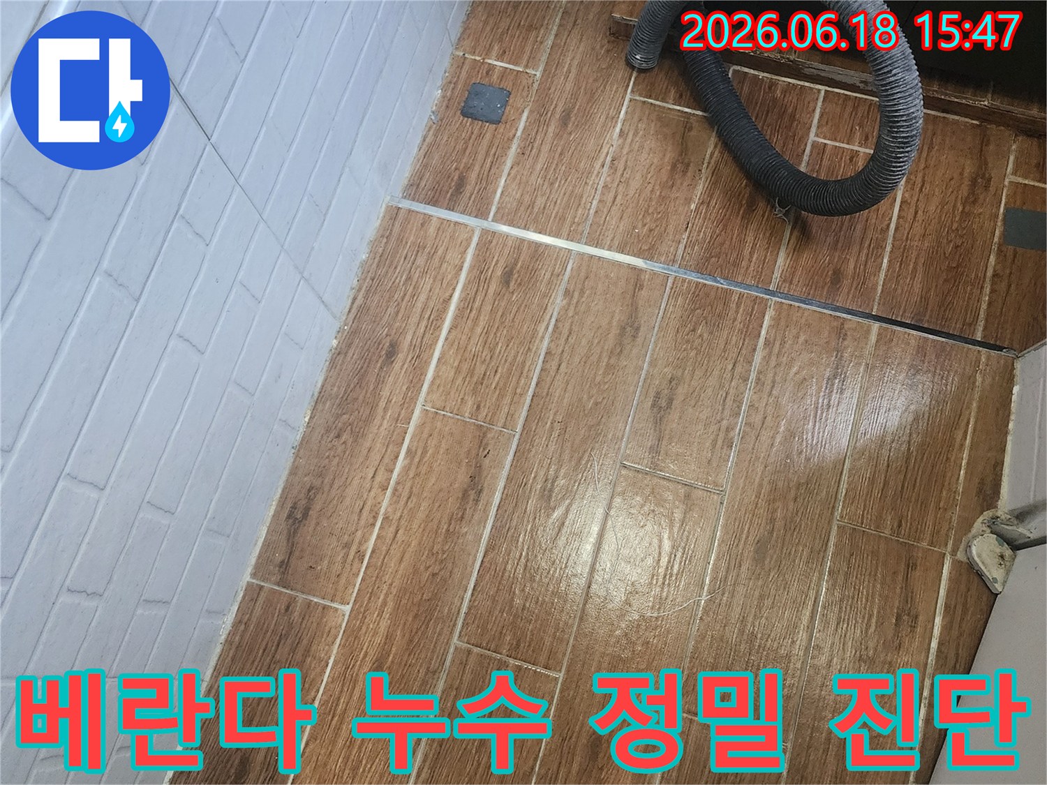 염창동 아파트 베란다에서 누수 의심으로 정밀 진단이 진행 중인 모습을 담은 사진입니다-바닥 타일 위에 탐지 장비의 일부인 호스가 놓여 있습니다.