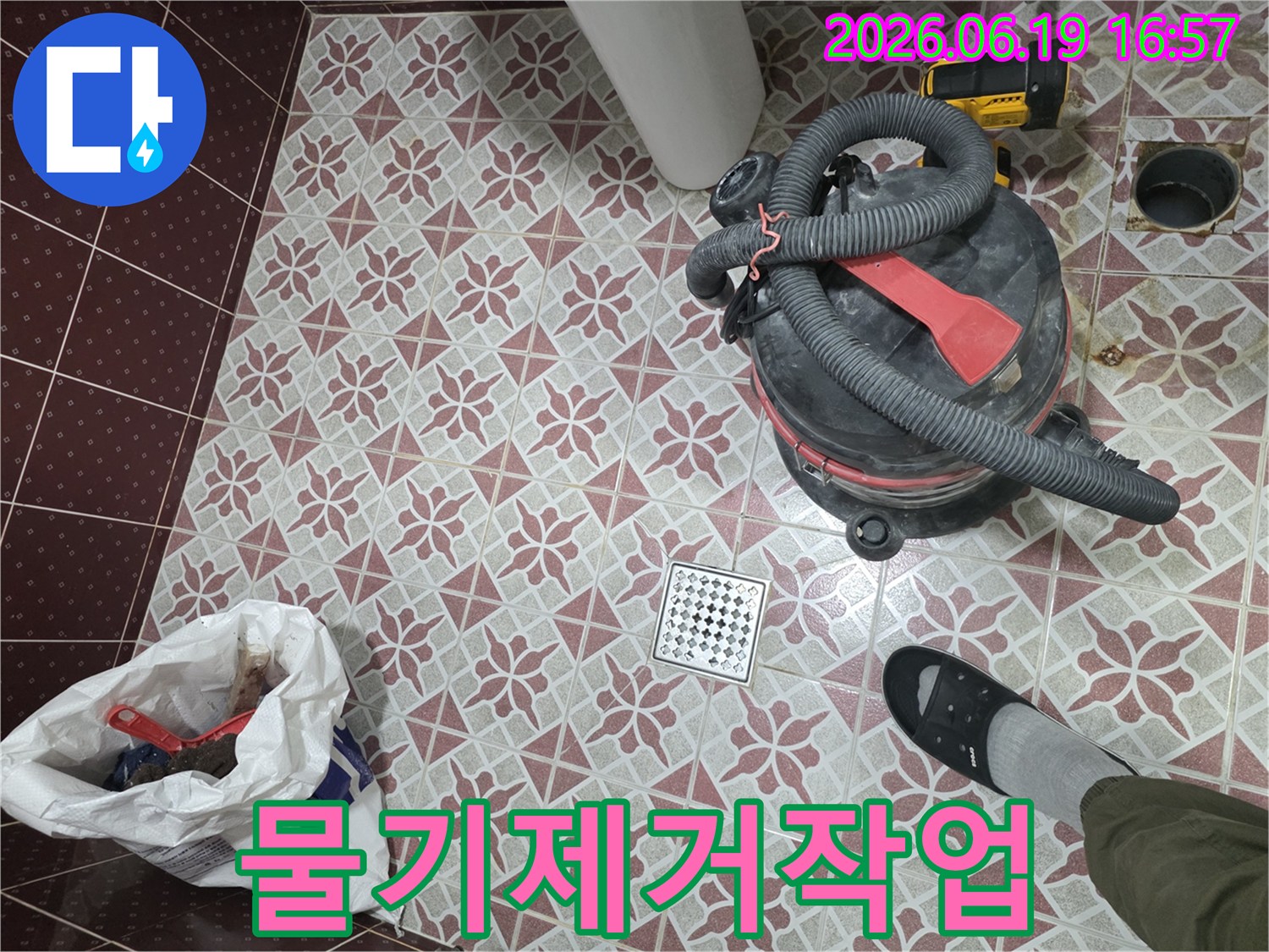 욕실 누수 복구 작업 중-바닥에 놓인 습식 청소기와-배수구-그리고 폐기물 봉투-작업의 진행 상황을 보여주는 이미지