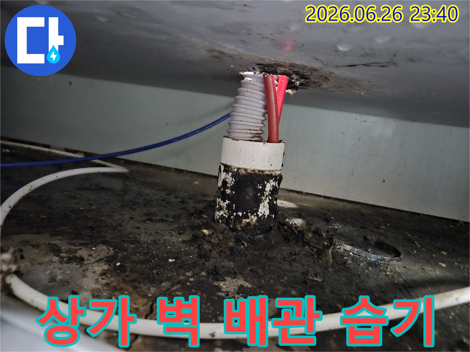 상가 벽면 배관 틈새에서 발생한 누수로 인해-주변에 심각하게 형성된 습기와 오염 흔적을 보여줍니다.