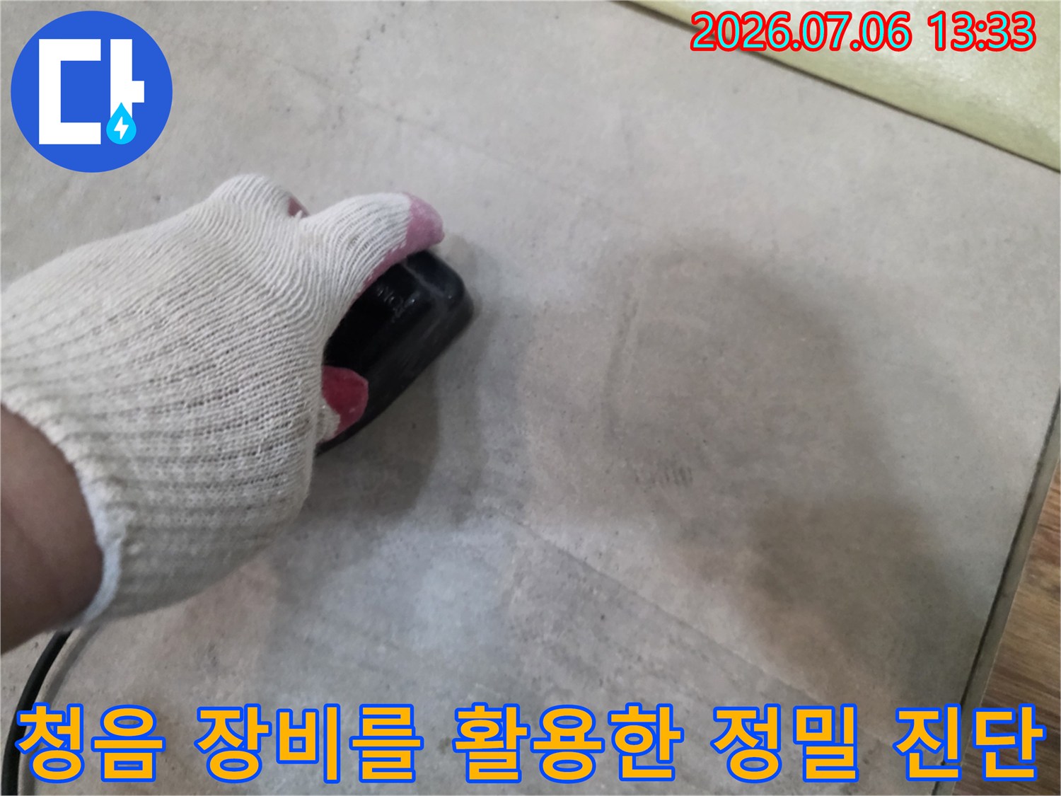 장갑을 낀 손으로 청음기 기기를 조작하며 바닥 아래 배관 파손 지점을 추적하는 장면