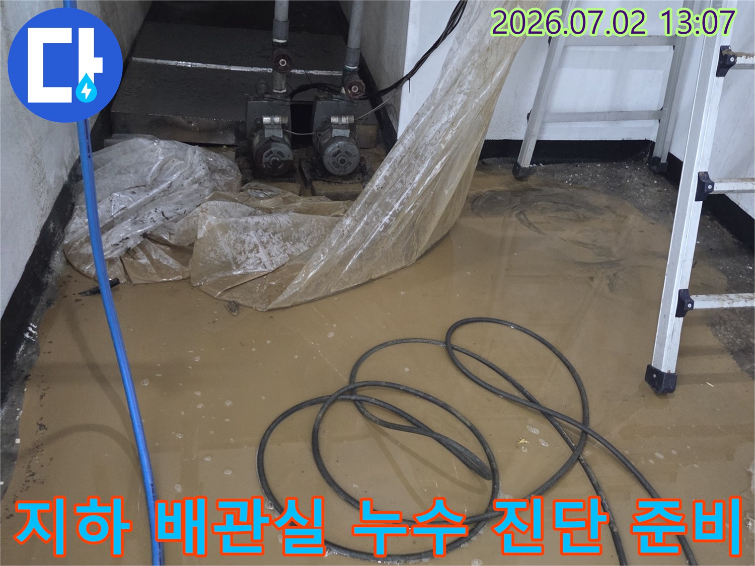 흰색 사다리가 세워져 있고 바닥에 파란 호스와 검은 선들이 엉켜 있는 지하 작업 현장