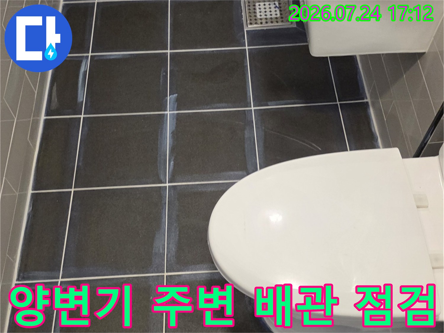 세면대와 양변기가 설치된 화장실 내 벽면 타일과 배수 공간의 모습