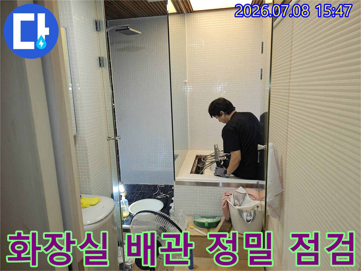 화장실 바닥 세면대 아래쪽에서 작업자가 배관 연결 부위를 세밀하게 점검하는 모습