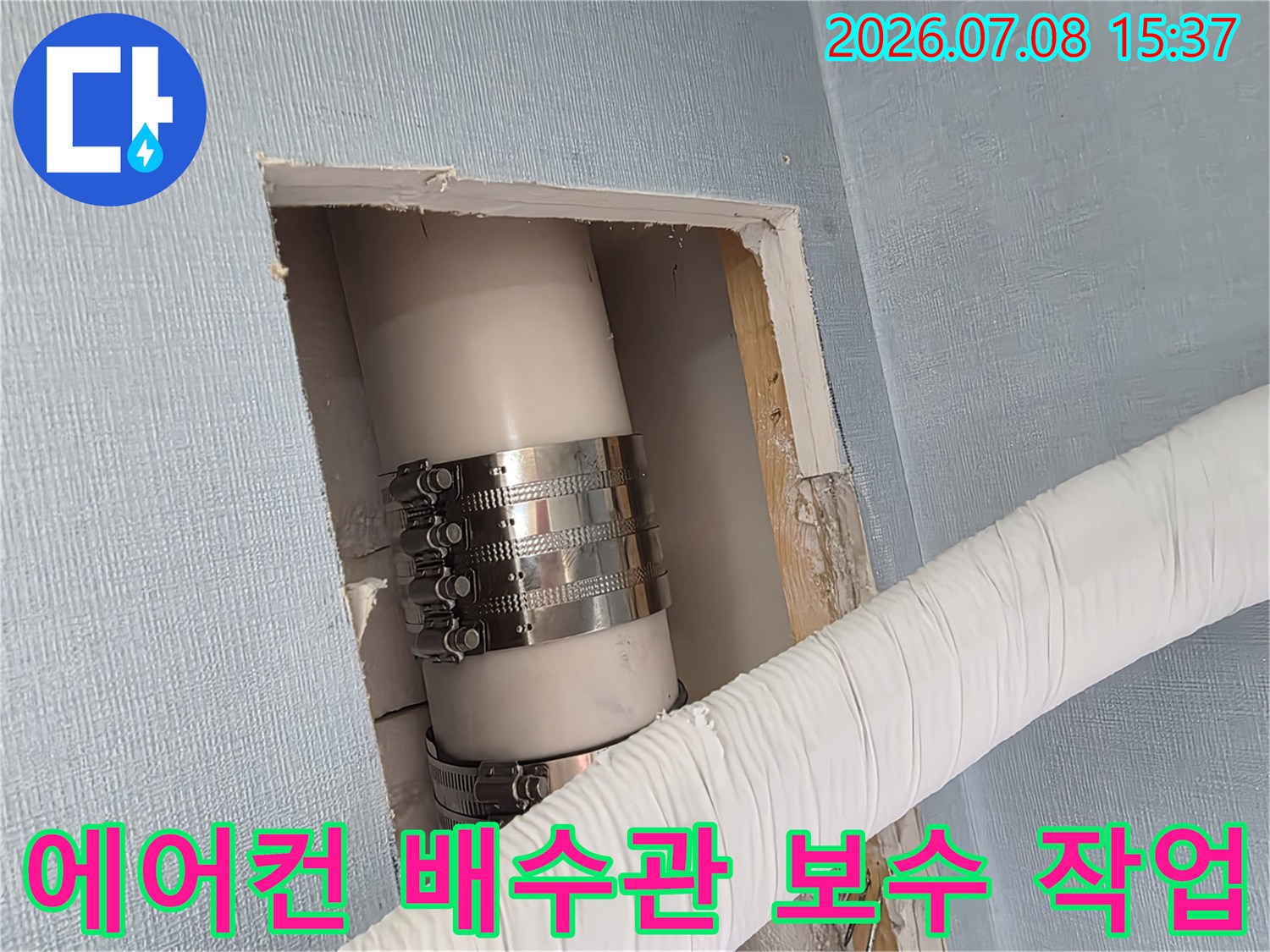 금속 밴드로 고정된 에어컨 드레인 배관과 하얀색 보호재가 감싸진 관이 벽면을 통과하는 모습