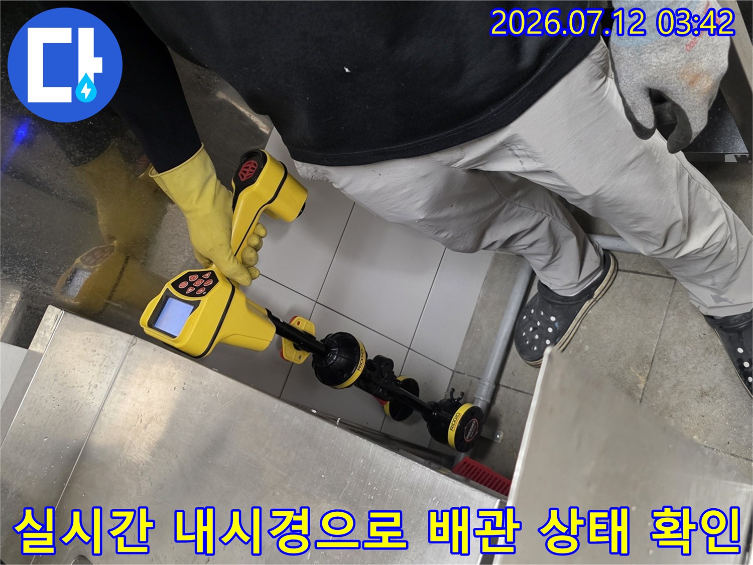 노란 장갑을 착용한 기술자가 트렌치 구역에서 전용 탐지기와 내시경을 사용하여 배수관 누수를 진단함