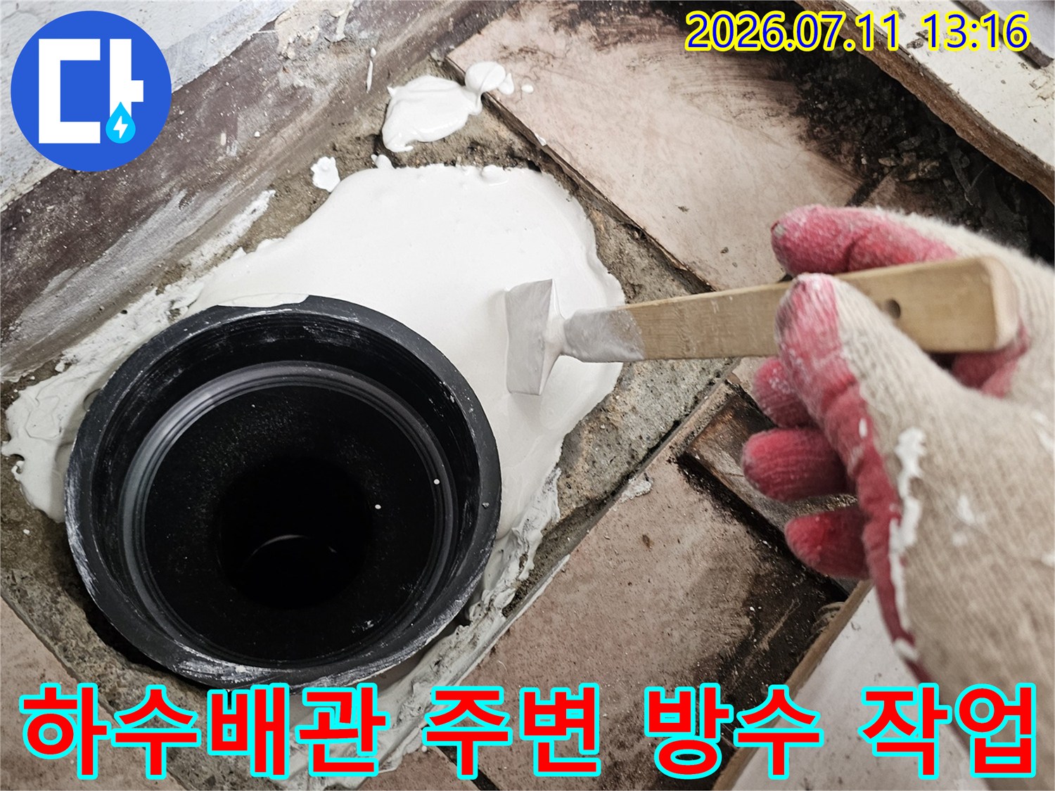 장갑을 낀 손이 헤라를 사용하여 하수 배관 주위의 틈새를 메우는 공사 현장