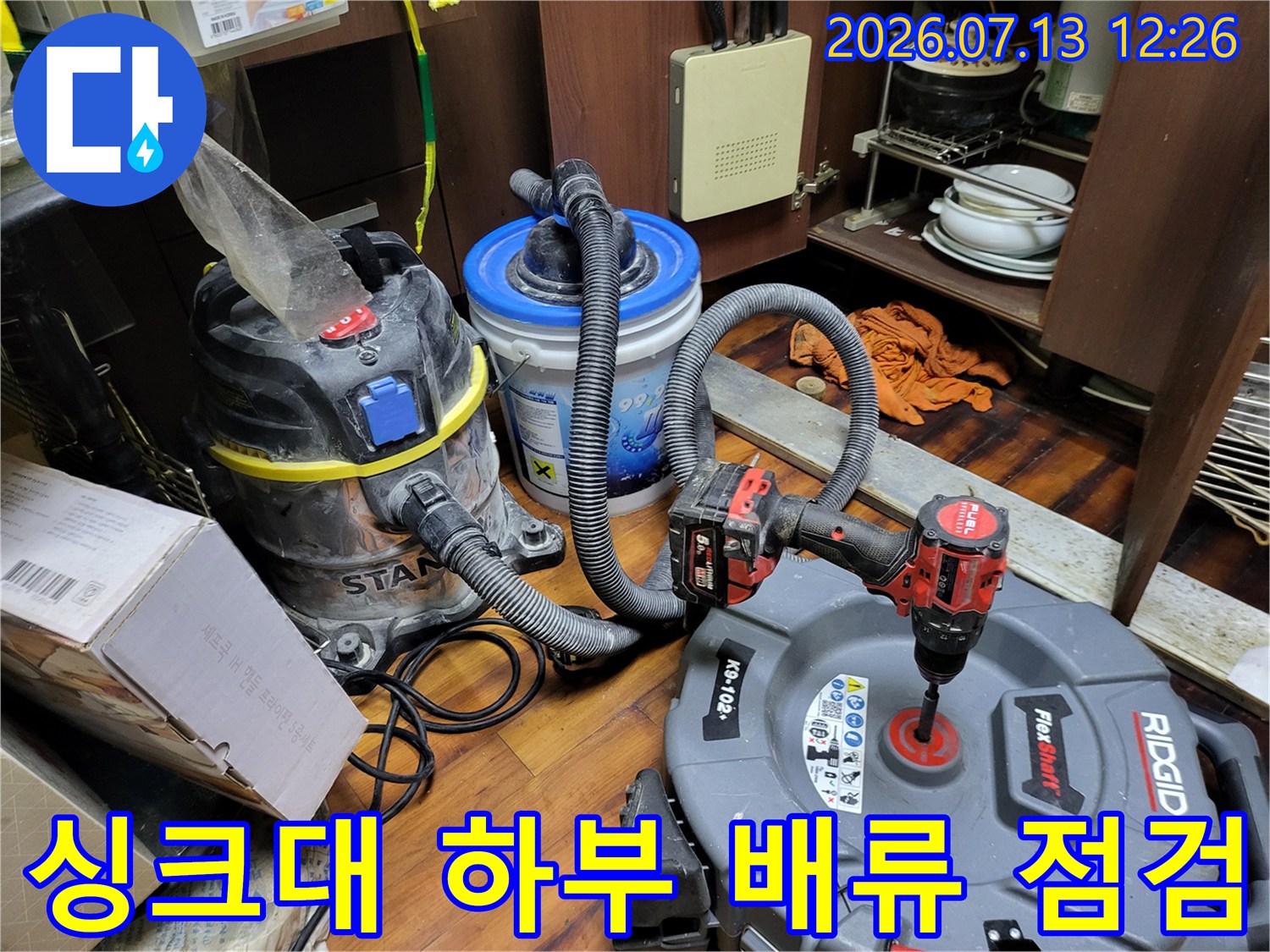 석션 장비와 세척 노즐을 연결하여 싱크대 밑 배수 시설을 집중적으로 관리하는 장면