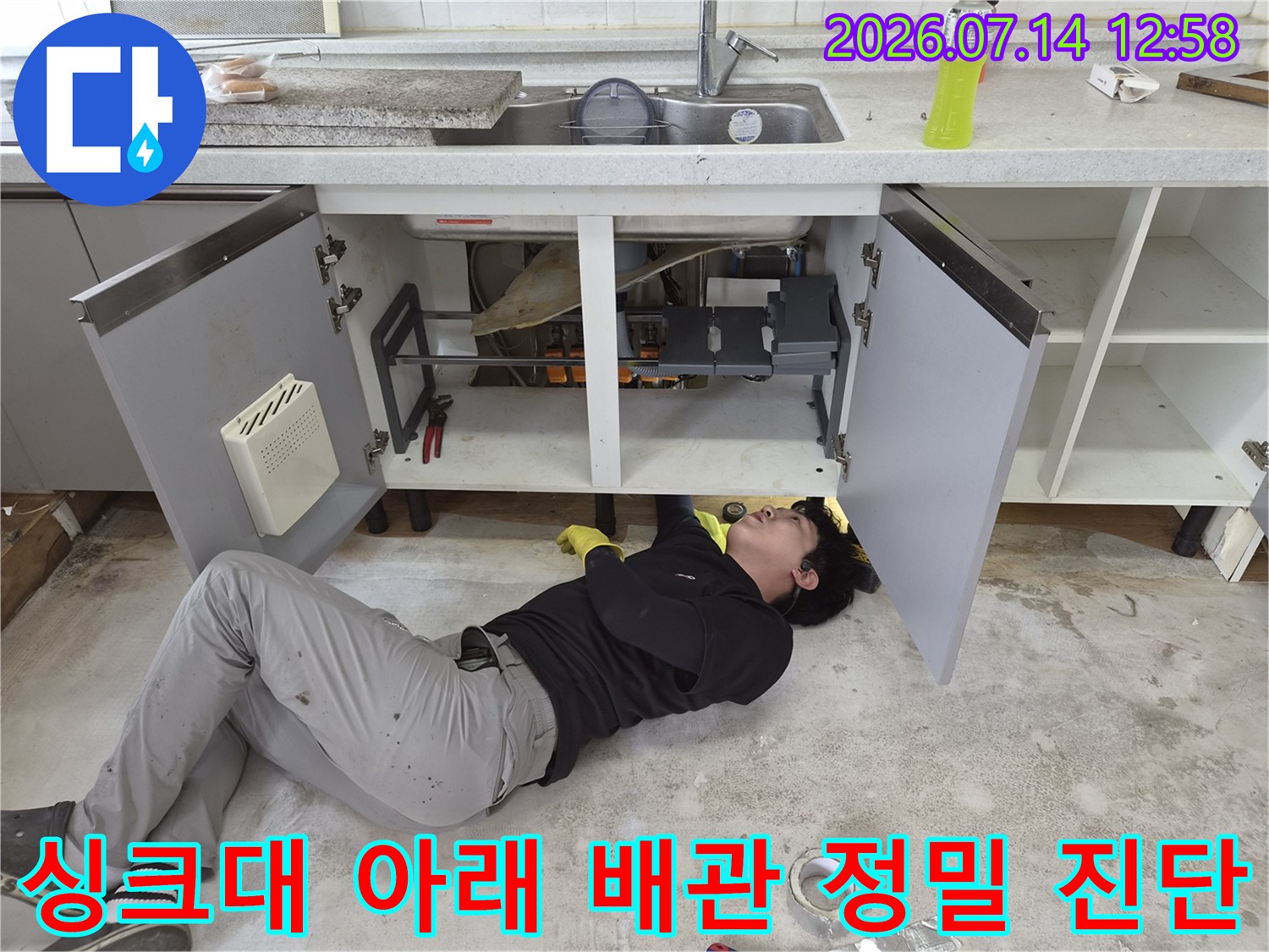 좁은 싱크대 하부장 내부에서 누수 지점을 찾기 위해 누워 있는 엔지니어