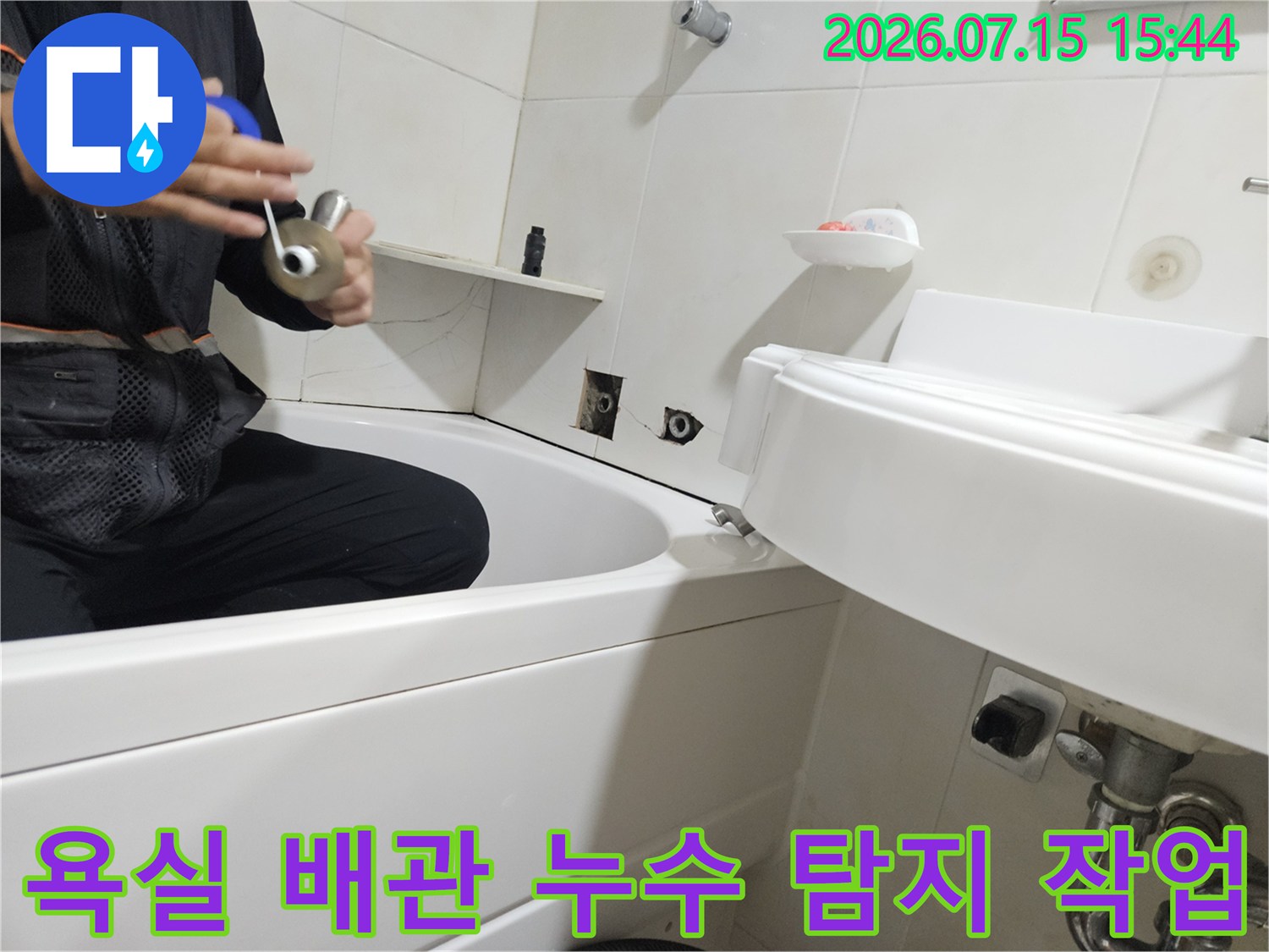 전문가가 세면대 하부 노출된 배관 부위를 청음 장비로 정밀 점검하는 모습
