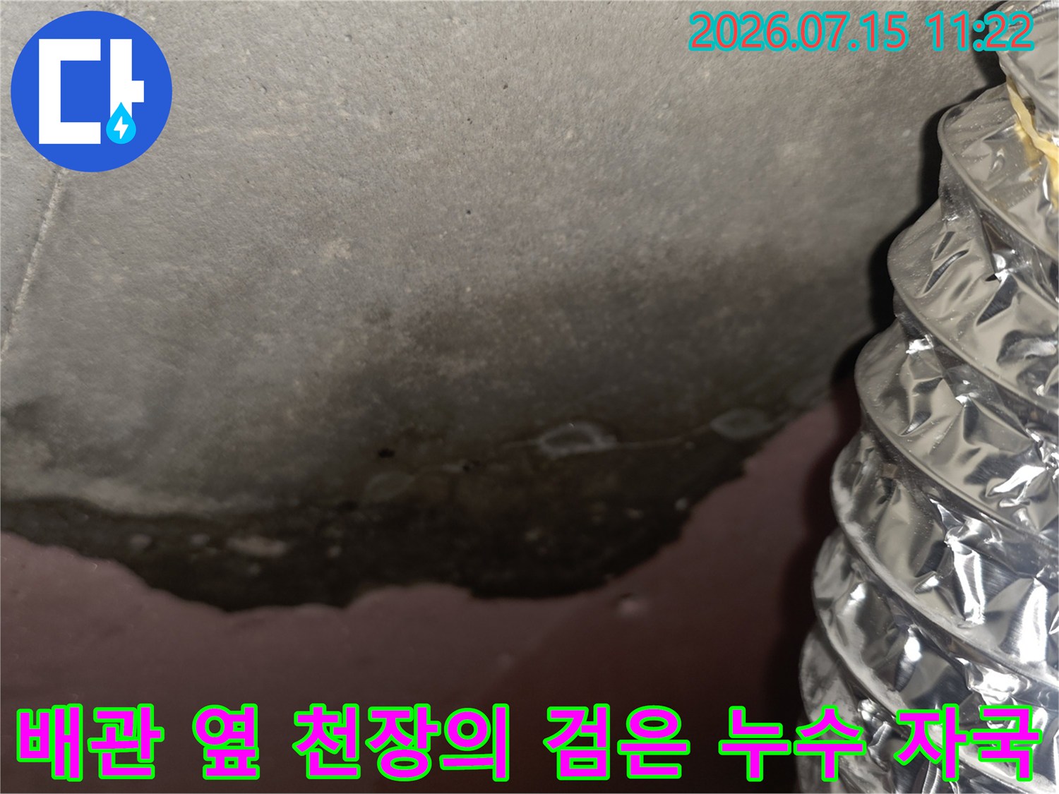 천장 마감재에 발생한 짙은 색의 누수 얼룩-그 옆으로 배치된 알루미늄 소재의 플렉시블 배관