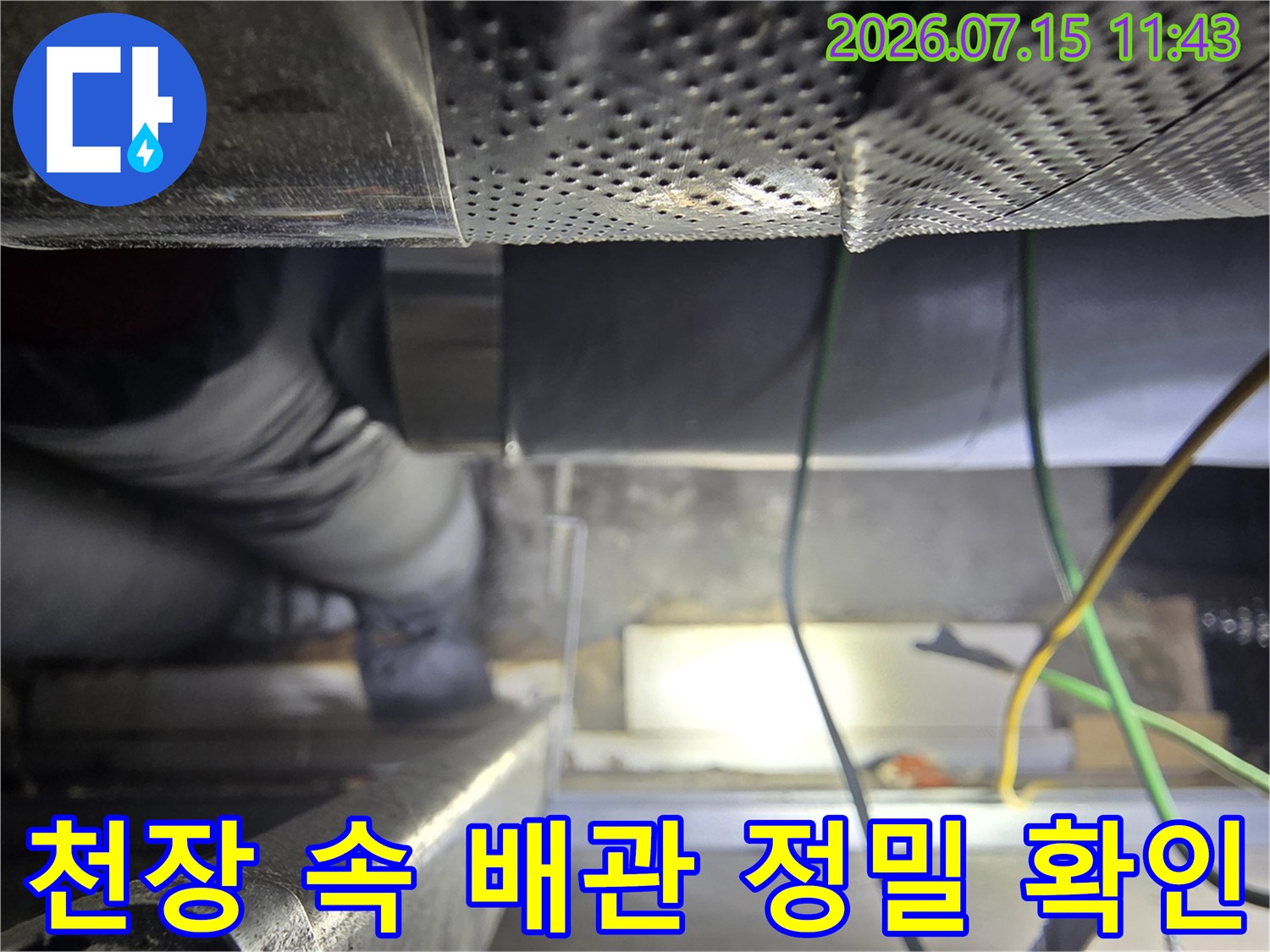 타공 마감재 아래-좁은 틈새 공간에서-보온재로 감싸진 배관을 살피는 모습